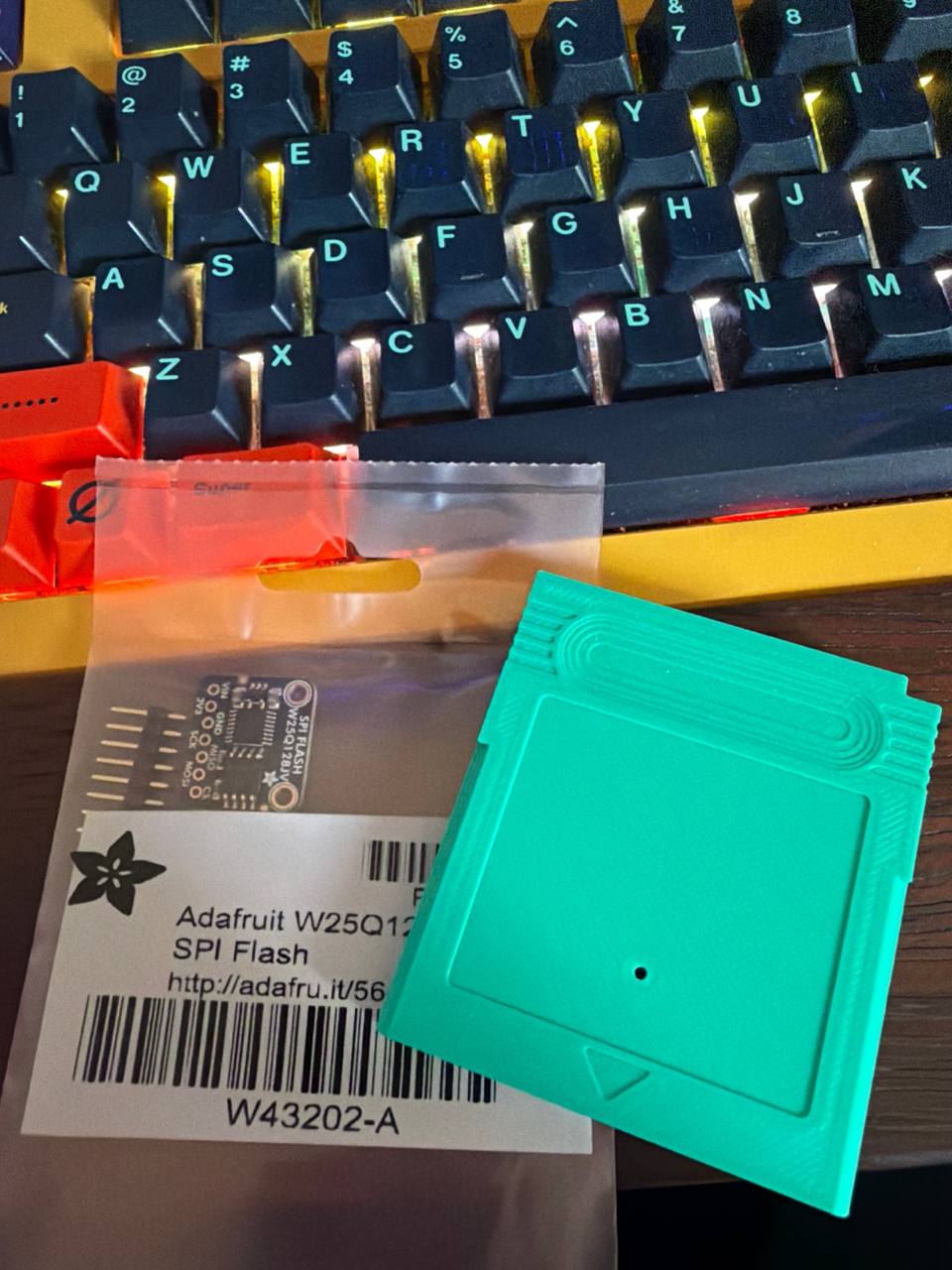 The W25Q128 flash breakout, still in its Adafruit bag, next to an empty Game Boy cartridge shell - 16 MiB of flash and the form factor I want to dock it into